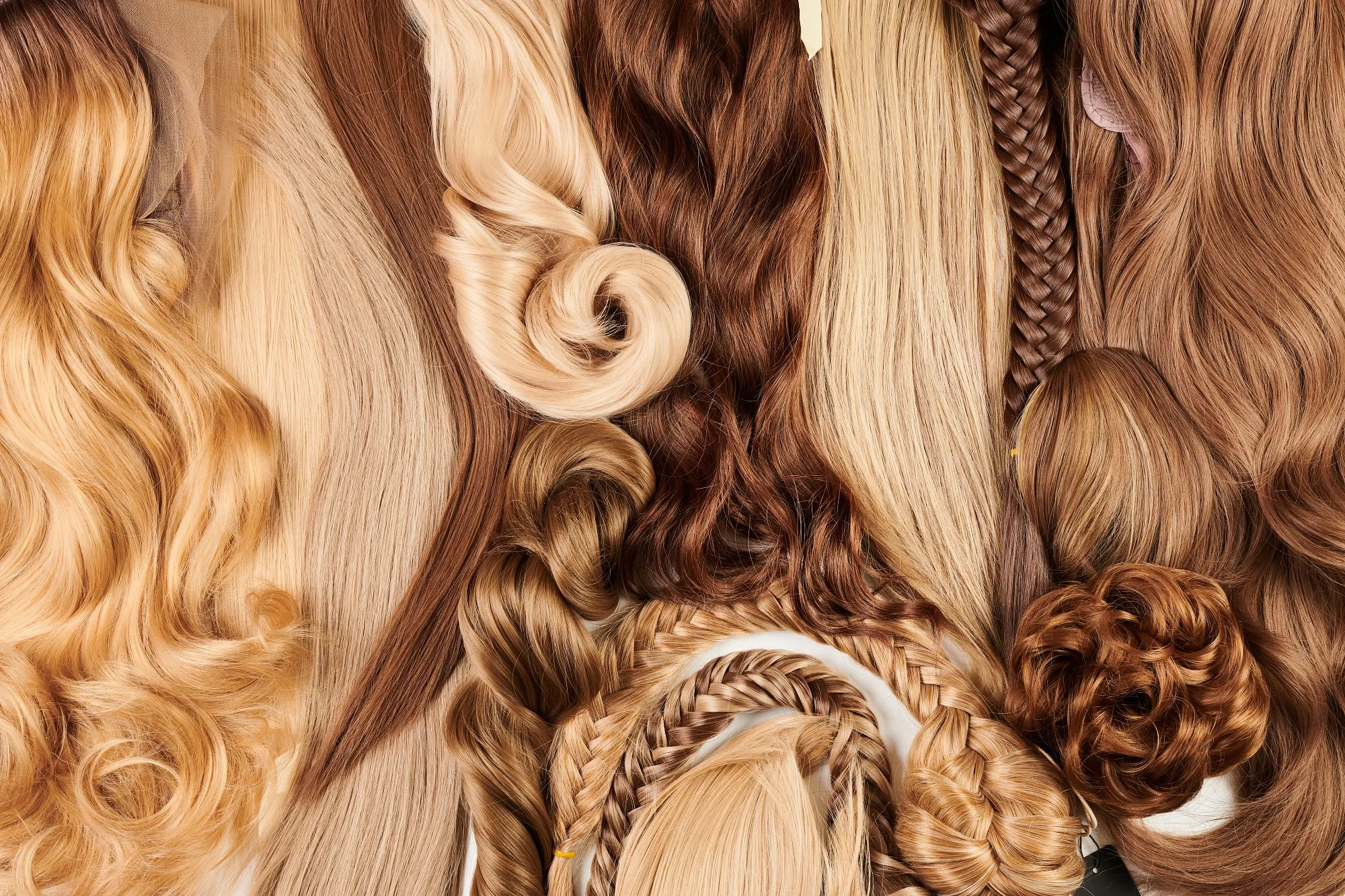 Bovenaanzicht van diverse haarstukken en extensions in blond-, karamel- en bruintinten, met golvende en stijle lengtes, vlechten en een knotje.